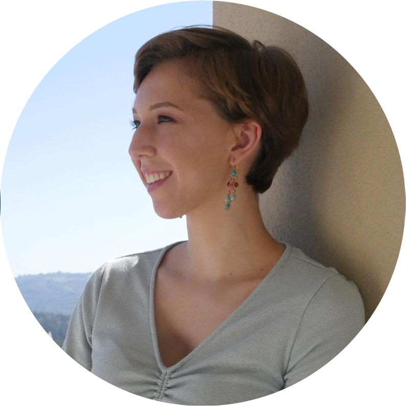 An image shows a photo of Natalie Gospe. They are smiling and looking off to the left side of the screen. Their hair is short, they are wearing earrings, and a blue shirt. Behind them is a blue skyline and a tan post.
